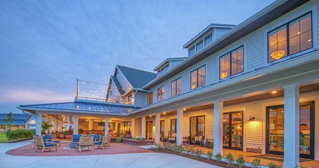Commercial building exterior featuring white siding, a covered walkway, and outdoor patio seating at Signature Bayside Clubhouse.