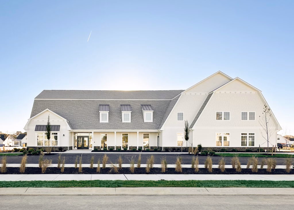 Large modern clubhouse exterior featuring a barn pitched roof, dormers, and white window frames.