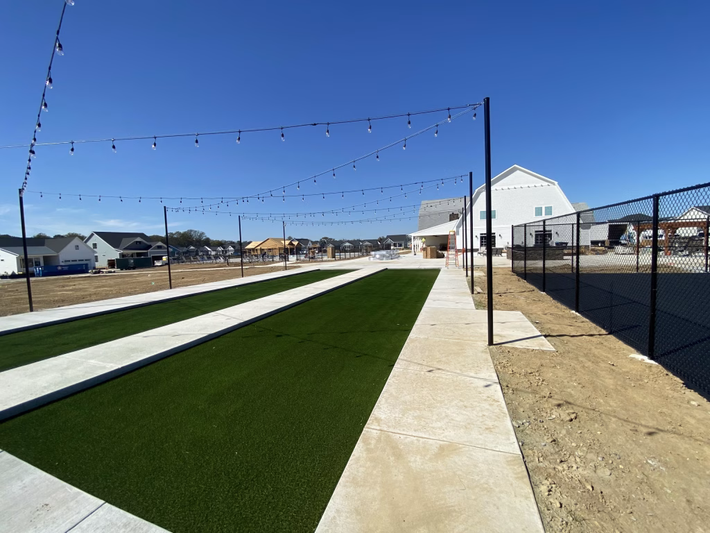 Large modern event space exterior featuring artificial turf courts, string lights, and a fenced patio at Towerhill Clubhouse.