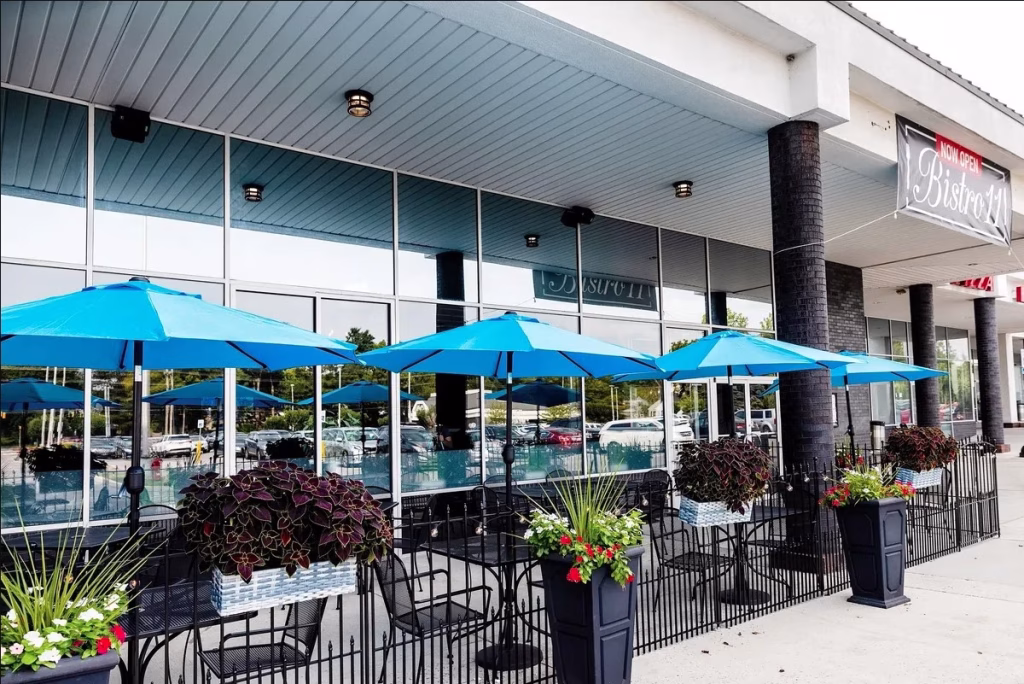 Bistro 11 exterior featuring a fenced outdoor dining patio, bright blue umbrellas, and planters.