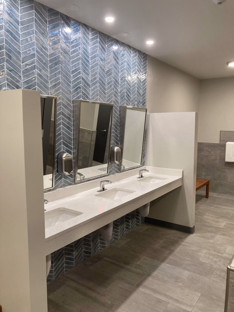 Modern commercial restroom design featuring a blue herringbone tile wall, sinks, and mirrors at Towerhill Clubhouse