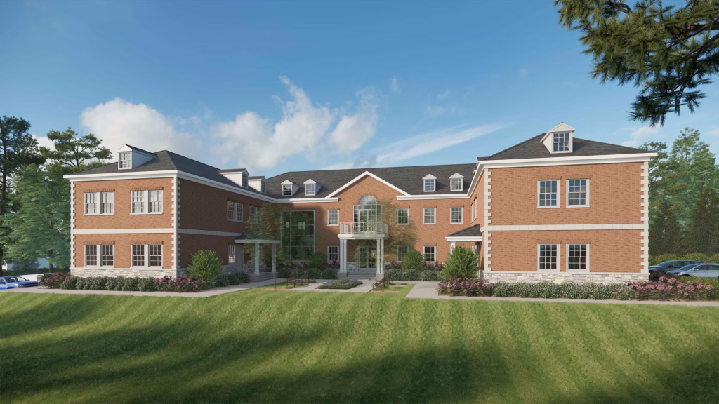 Large student dorm exterior featuring a red brick facade, dormer windows, and a manicured lawn.